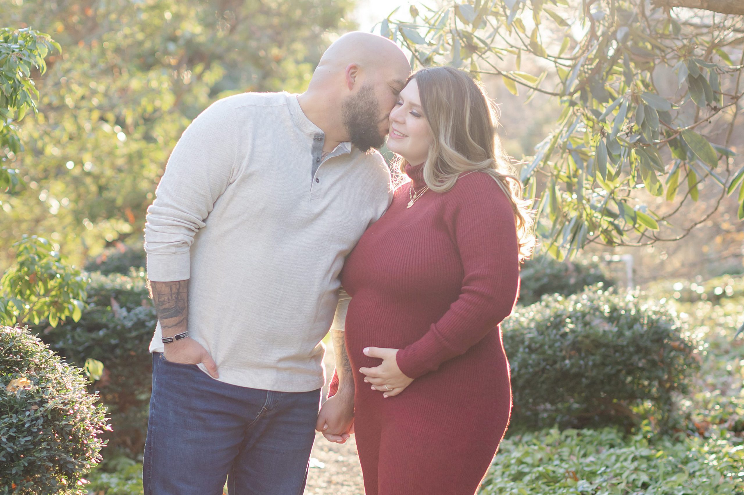 Husband kisses pregnant wife's cheek at Cross Estate Gardens in NJ.
