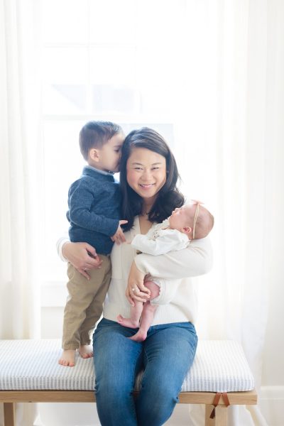 A mom holding her baby daughter smiles while her young son kisses her head in Westfield NJ.