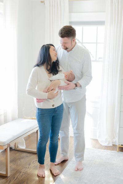 A mom and dad look at each other while holding their baby daughter standing in their bedroom in Westfield NJ.