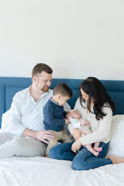 A family of four sits on a bed looking down at the baby sister in Westfield NJ.