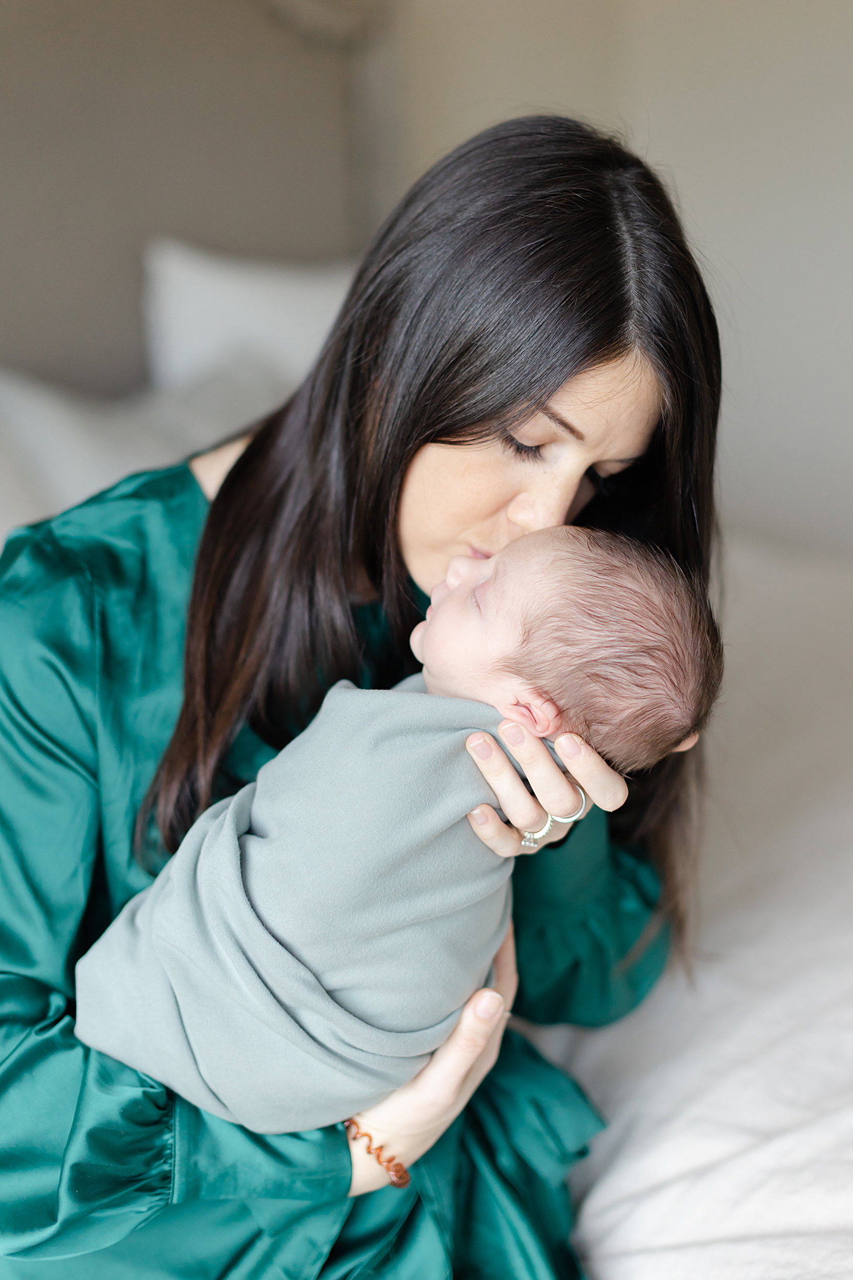 Mom wearing green dress kiss newborn son on his cheek.