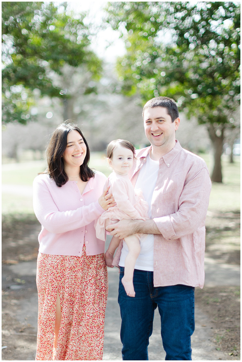 Mom and dad smile and walk with their daughter at Taylor Park in Millburn NJ for family photos.